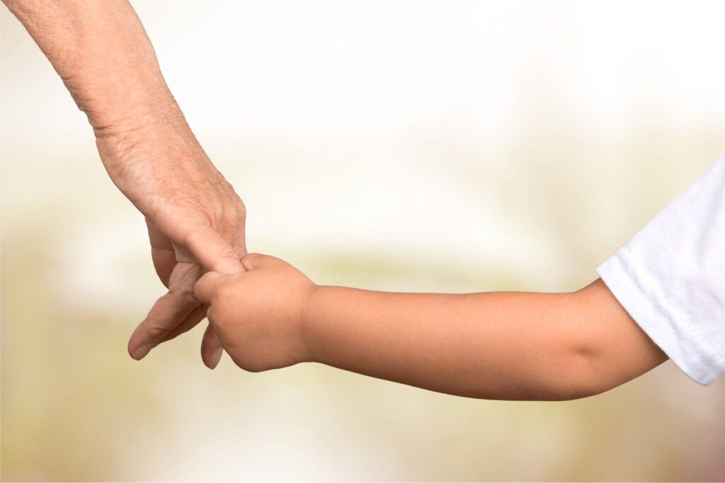 A small child holding the pinky of an adult.
