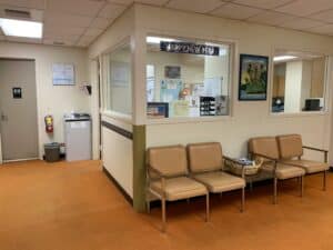 Medical clinic waiting room with reception window and row of beige chairs